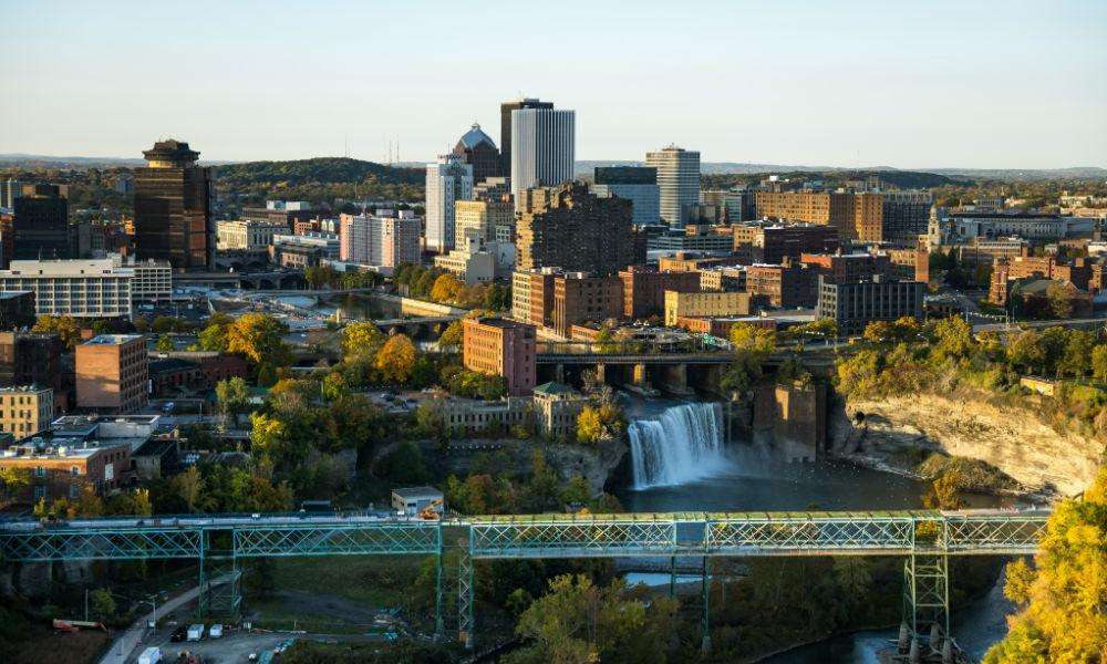 A panoramic view of Rochester from a hilltop, showcasing the skyline and urban landscape, with the University of Rochester nearby.